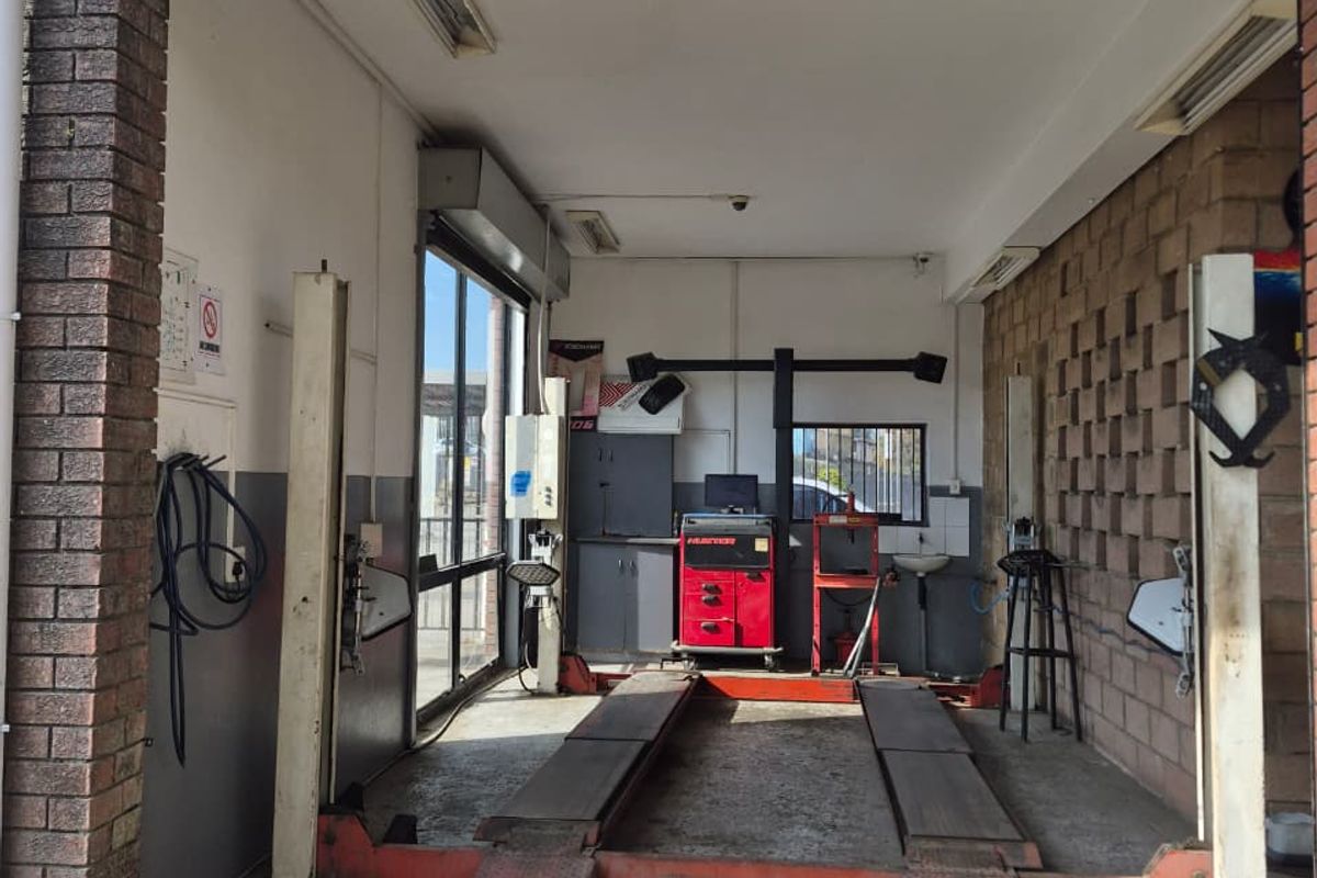 Industrial garage bay featuring a built-in vehicle lift, exposed brick walls, and functional lighting, suitable for automotive maintenance or workshop use.