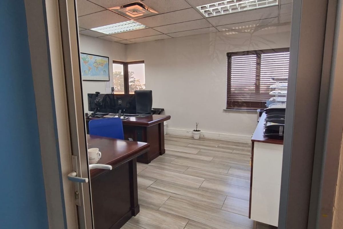 A functional office space featuring wood-look tile flooring, a suspended ceiling with recessed lighting, and large windows with venetian blinds.