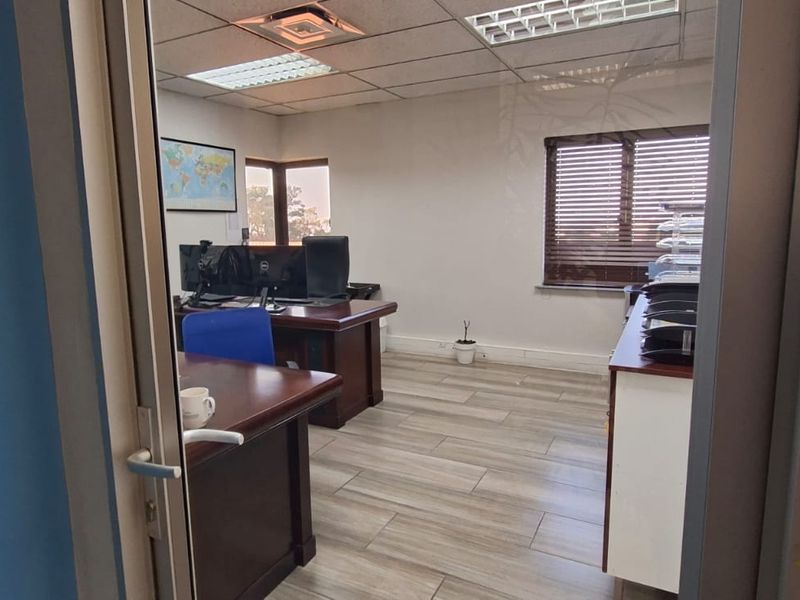A functional office space featuring wood-look tile flooring, a suspended ceiling with recessed lighting, and large windows with venetian blinds.