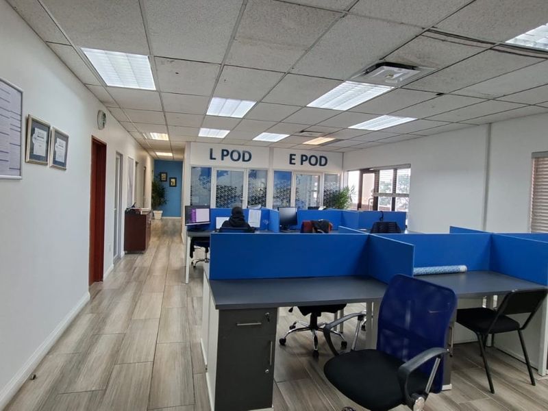 Open-plan office space featuring modular cubicle workstations, wood-look tile flooring, and a suspended ceiling with recessed lighting.