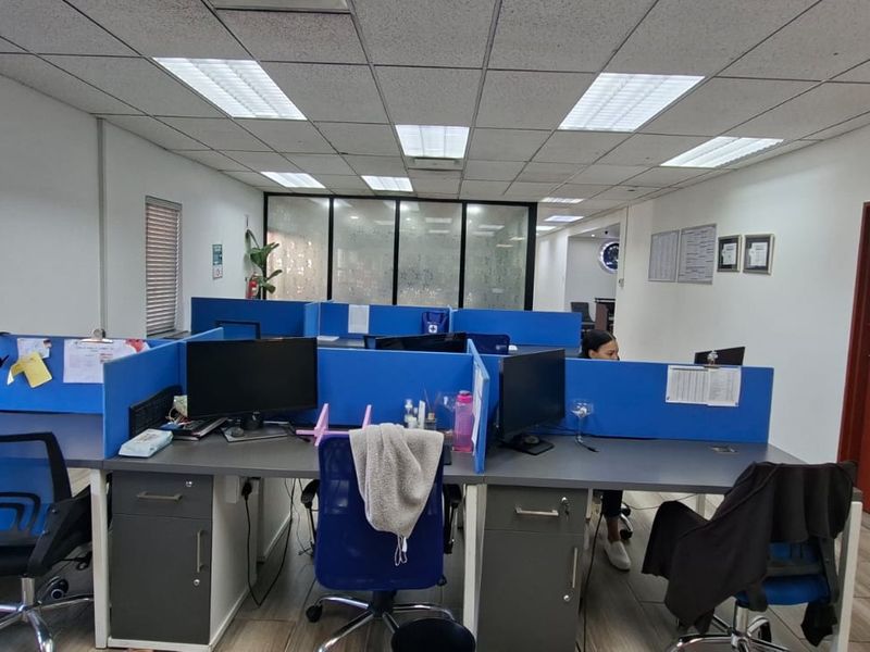 A functional office space featuring a suspended ceiling with recessed lighting, laminate flooring, and glass partition walls, configured with multiple workstations.