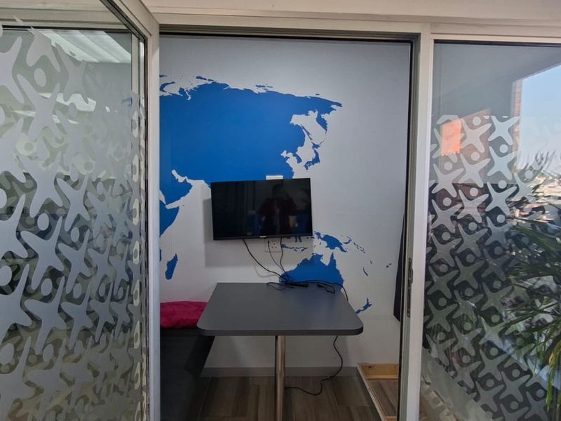 A compact office space featuring a glass partition, wood-look vinyl flooring, and a wall-mounted television against a decorative world map wall.