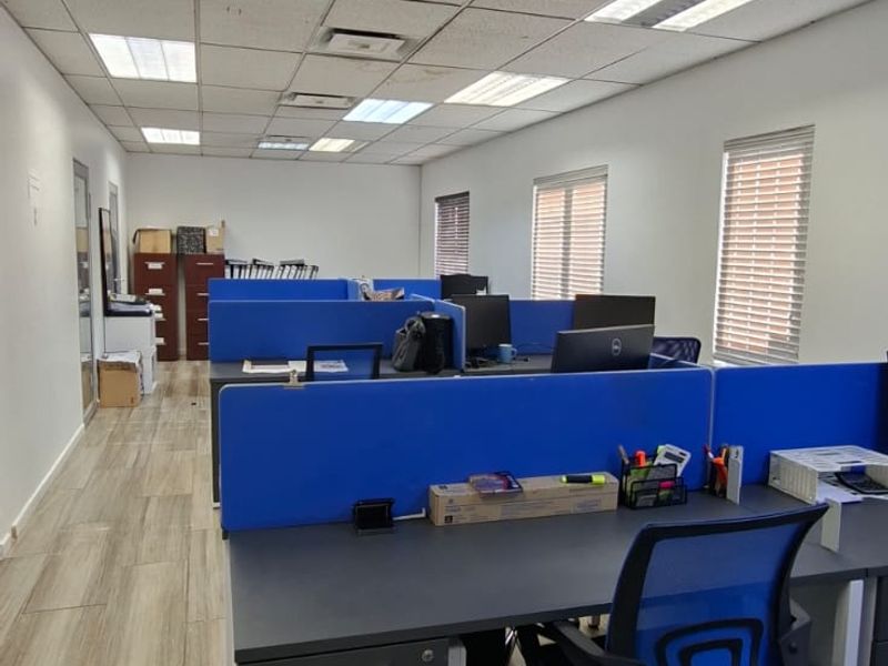 Open-plan office space featuring wood-look tile flooring, recessed lighting, and suspended ceiling tiles with integrated air conditioning vents.