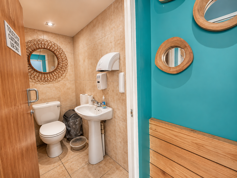 A clean, functional restaurant restroom featuring tiled walls and flooring, a pedestal sink, and wall-mounted utility fixtures.