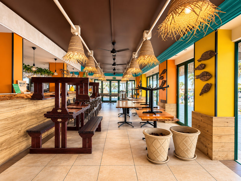 Spacious open-plan restaurant interior featuring tiled flooring, ceiling fans, and large glass sliding doors leading to an outdoor area.