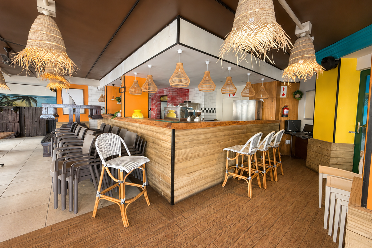 A vibrant restaurant interior featuring a prominent wooden bar counter, mixed flooring, and decorative pendant lighting, creating a casual dining atmosphere.