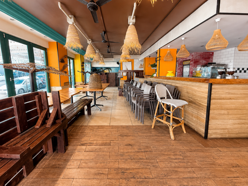 Open plan restaurant interior featuring a wooden bar counter, tiled flooring, decorative pendant lighting, and large bi-fold doors providing natural light.