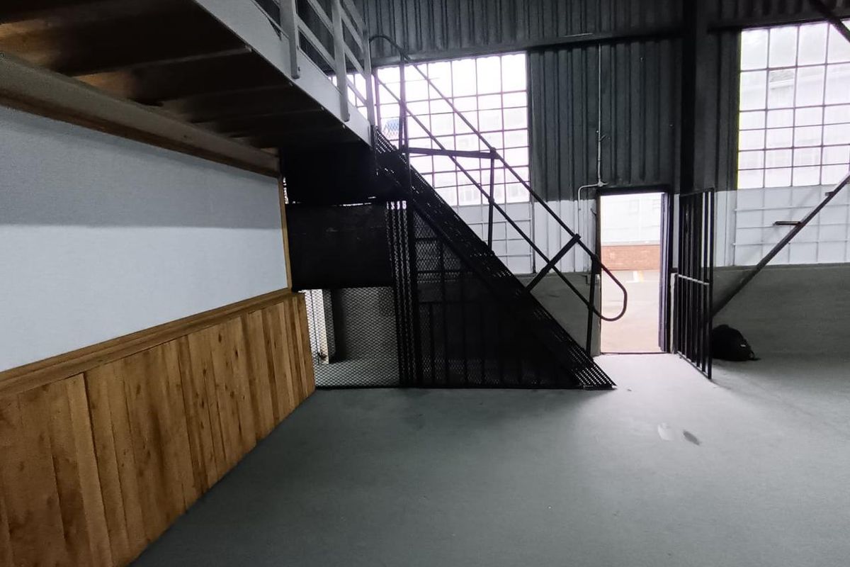 Industrial utility space featuring a mezzanine level, metal staircase, large steel-framed windows, and durable concrete flooring with timber wall paneling.