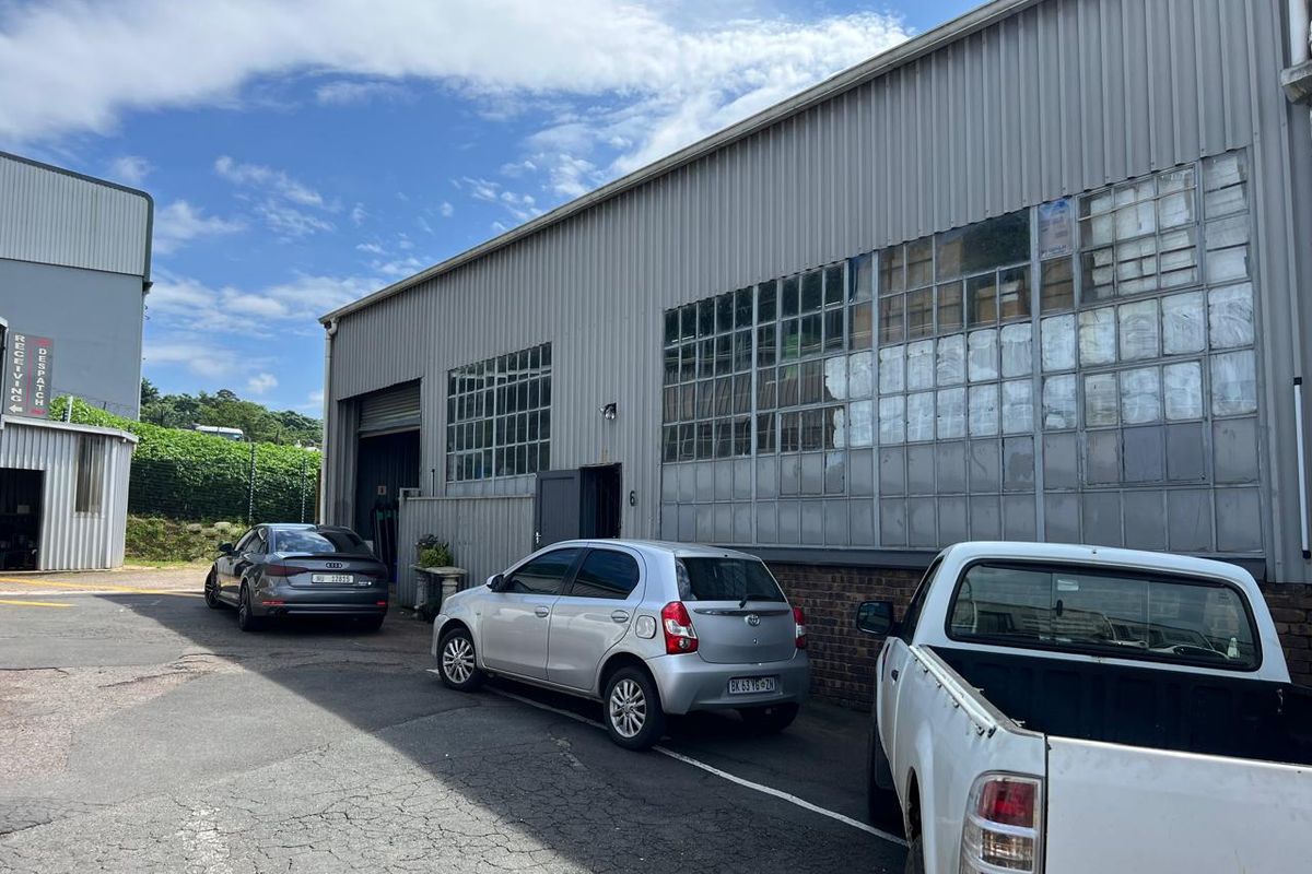 Exterior view of an industrial warehouse facility featuring corrugated metal cladding, large steel-framed windows, and a roller shutter door access point.