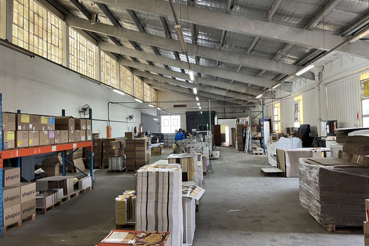 Spacious industrial warehouse facility featuring high ceilings with exposed steel trusses, concrete flooring, and ample natural light through clerestory windows.