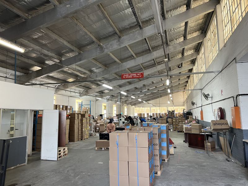 Spacious industrial warehouse facility featuring high-clearance ceilings with exposed steel trusses, concrete flooring, and functional overhead lighting suitable for storage or manufacturing operations.