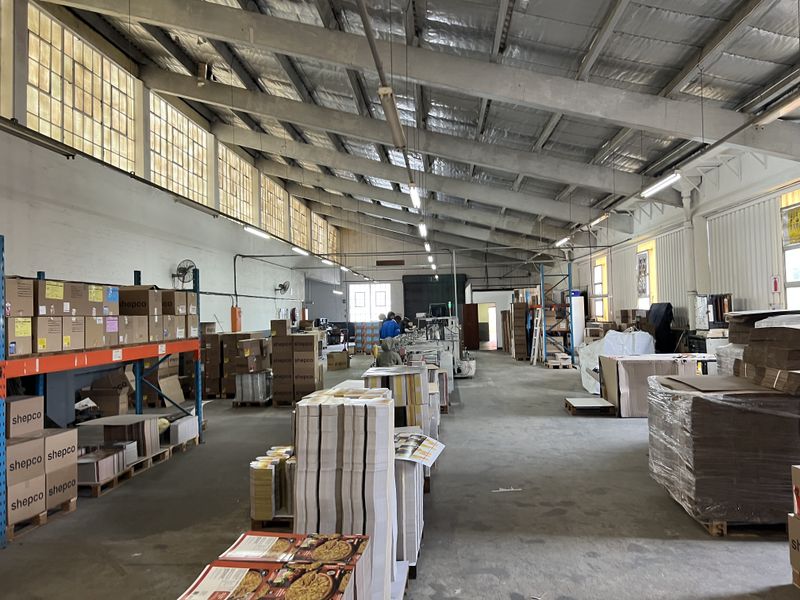 Spacious industrial warehouse facility featuring high ceilings with exposed steel trusses, concrete flooring, and ample natural light through clerestory windows.