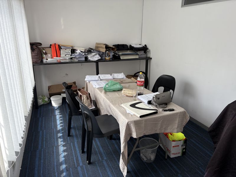 A functional office space featuring carpeted flooring and vertical window blinds, currently utilized as a workspace.