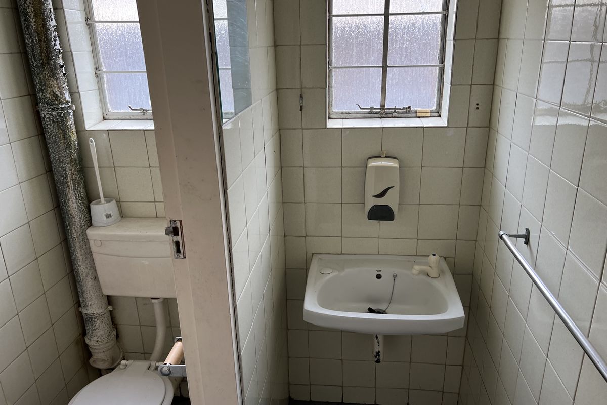 A dated office restroom featuring wall-mounted basin, toilet, and tiled walls, currently in need of refurbishment and modernization.