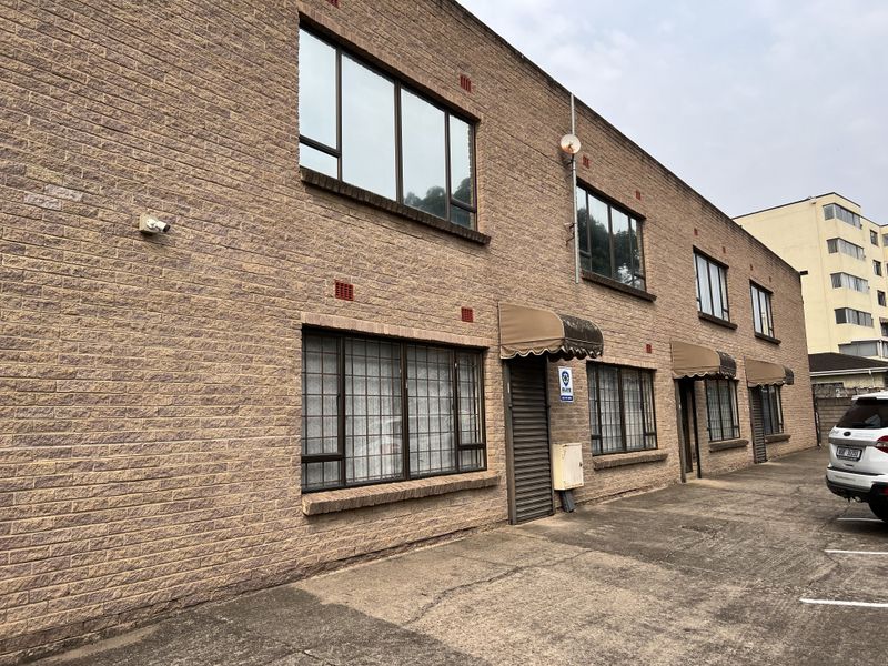 Exterior view of a two-story office building featuring face brick construction, aluminium windows with security bars, and canvas awnings over the entrances.
