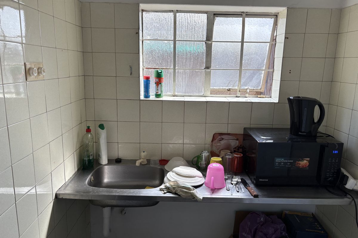 A compact kitchen area featuring a stainless steel sink, tiled splashback, and a metal-framed window, requiring cosmetic updates to improve the overall finish.