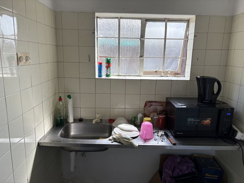 A compact kitchen area featuring a stainless steel sink, tiled splashback, and a metal-framed window, requiring cosmetic updates to improve the overall finish.