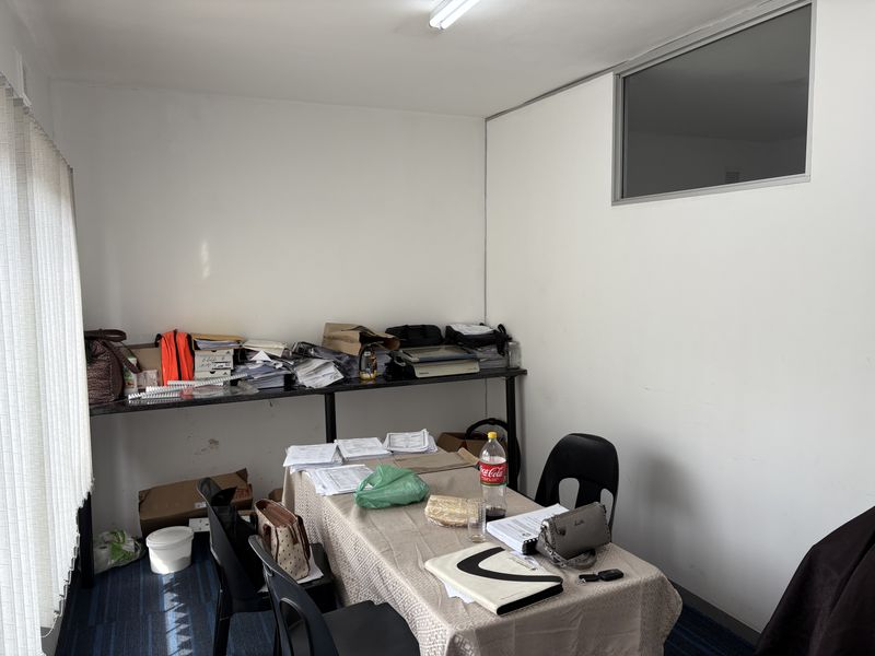 A functional office space featuring carpeted flooring, vertical blinds, and a transom window, providing a practical work environment.