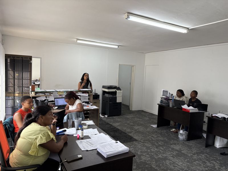 A functional office space featuring carpeted flooring, fluorescent lighting, and a security gate at the entrance.