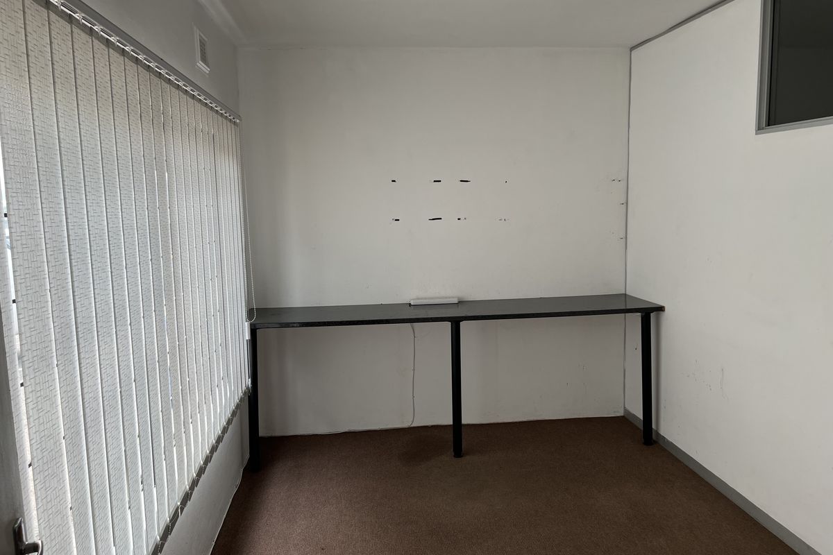 A vacant office space featuring a built-in desk, carpet flooring, and vertical blinds, requiring minor cosmetic repairs to the walls.