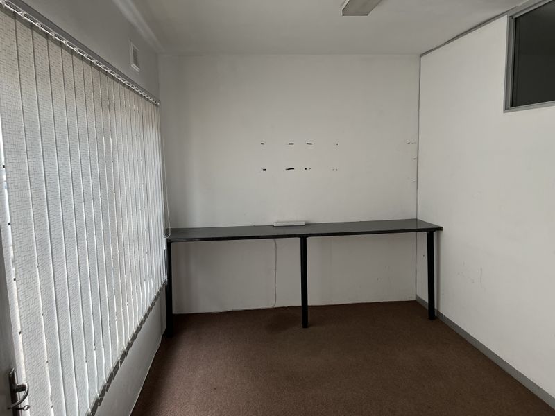 A vacant office space featuring a built-in desk, carpet flooring, and vertical blinds, requiring minor cosmetic repairs to the walls.