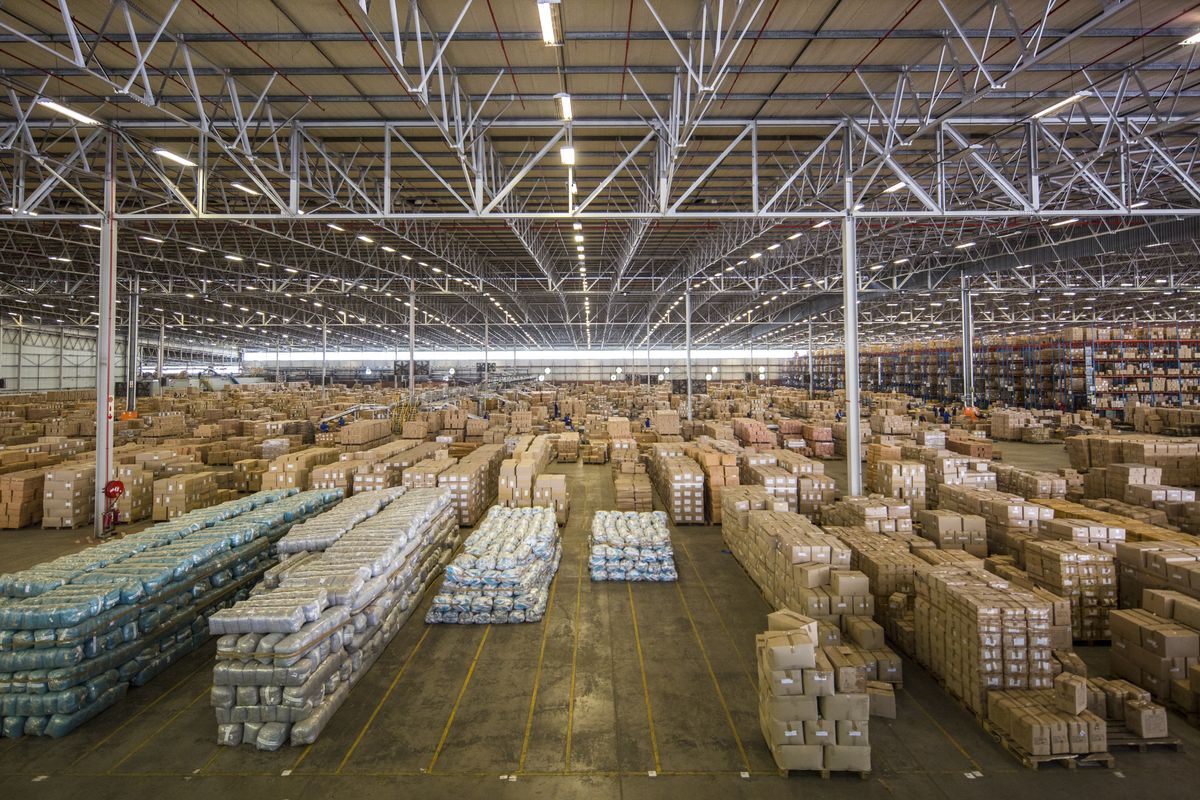 Large-scale industrial warehouse facility featuring high-clearance steel truss roofing, industrial lighting, and durable concrete flooring, currently utilized for bulk storage.