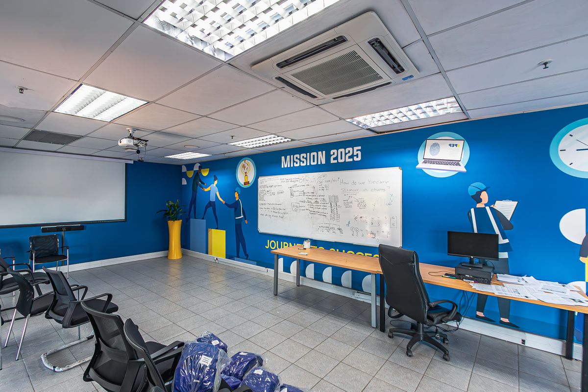 A functional office or training room featuring ceramic tile flooring, a suspended ceiling with integrated air conditioning, a projector screen, and a wall-mounted whiteboard.