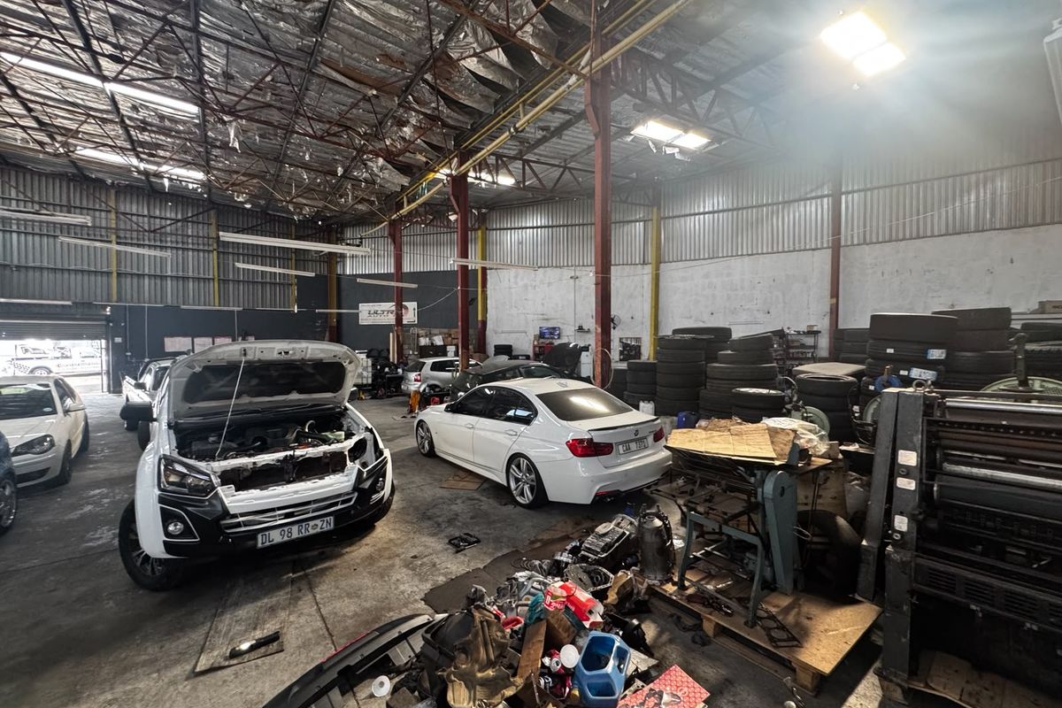 Spacious industrial workshop or garage featuring high ceilings with exposed steel trusses, concrete flooring, and ample space for vehicle maintenance and storage.
