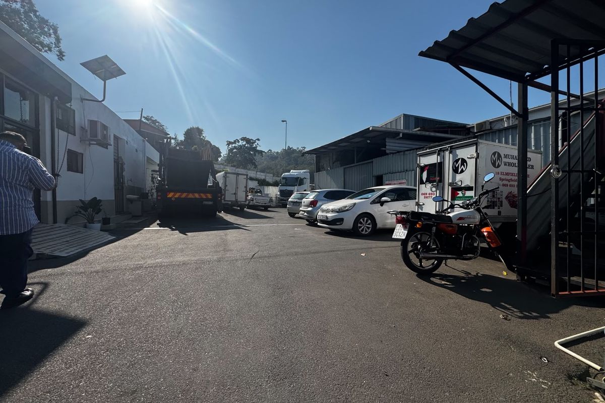 Industrial yard area featuring asphalt paving, a metal roof canopy, and external building infrastructure, providing functional space for logistics and vehicle access.