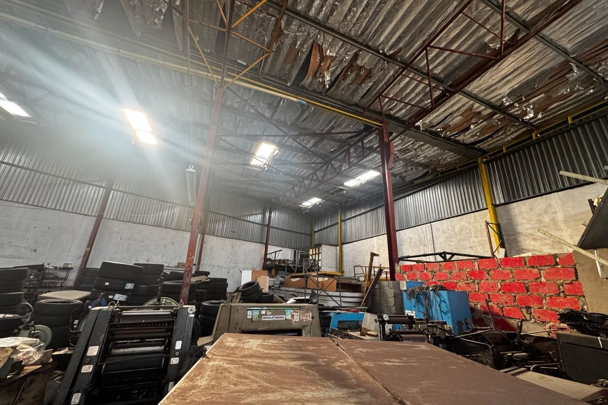 Industrial warehouse space featuring high ceilings with exposed steel trusses, corrugated metal roofing, and industrial lighting, suitable for storage or manufacturing operations.