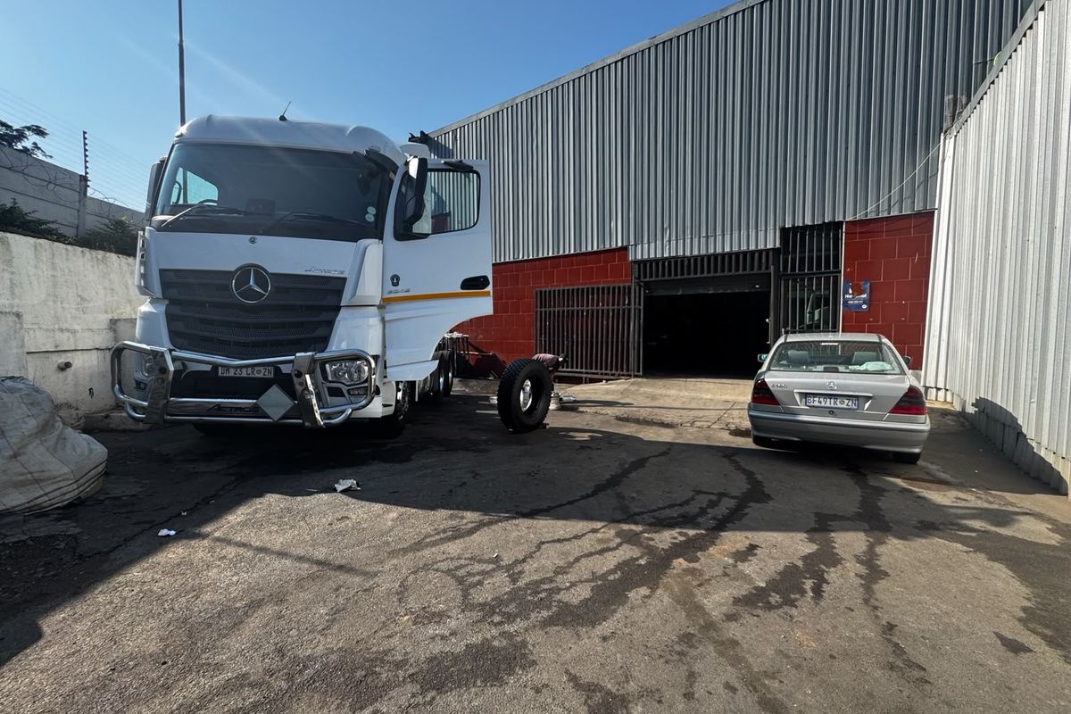 Industrial yard area featuring corrugated metal cladding, a large roller shutter door, and concrete hardstand suitable for heavy vehicle access.