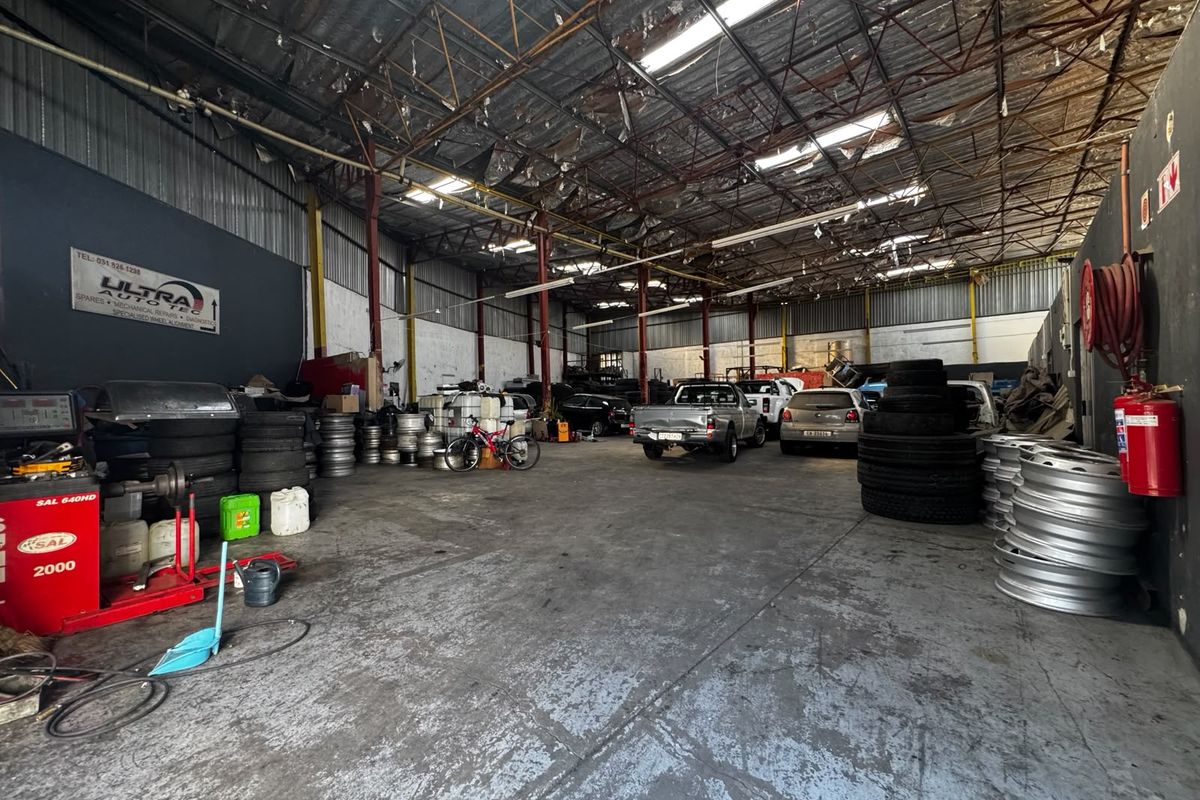 Spacious industrial workshop area featuring high ceilings with exposed steel trusses, skylights, and durable concrete flooring, suitable for automotive or light industrial operations.
