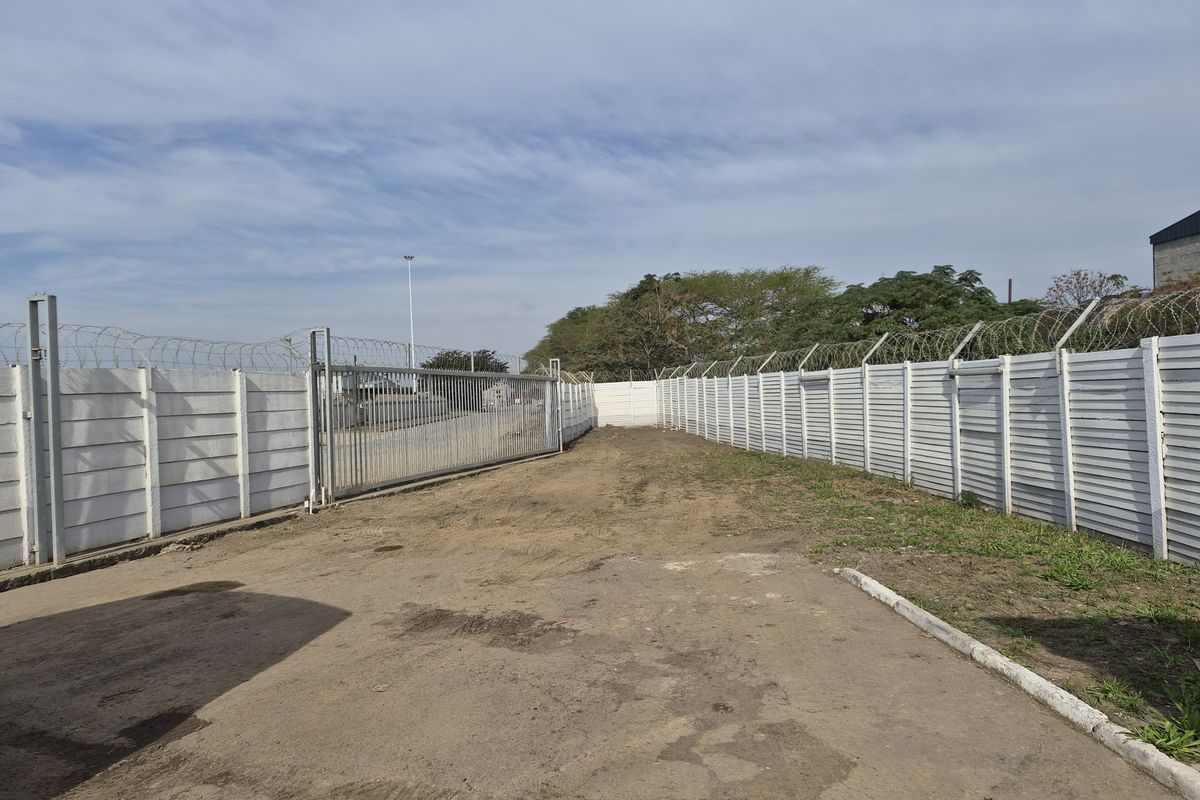 A vacant commercial land plot featuring secure perimeter precast concrete walling, razor wire fencing, and a large sliding steel access gate.