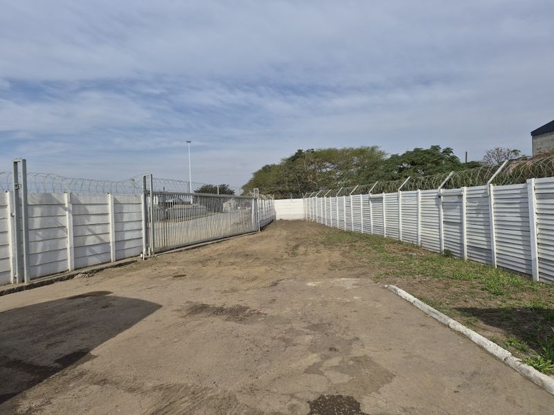 A vacant commercial land plot featuring secure perimeter precast concrete walling, razor wire fencing, and a large sliding steel access gate.