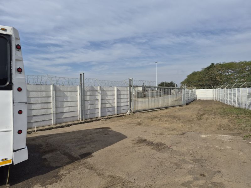 A secure commercial vacant land plot featuring a precast concrete perimeter wall topped with razor wire and a large sliding steel access gate.