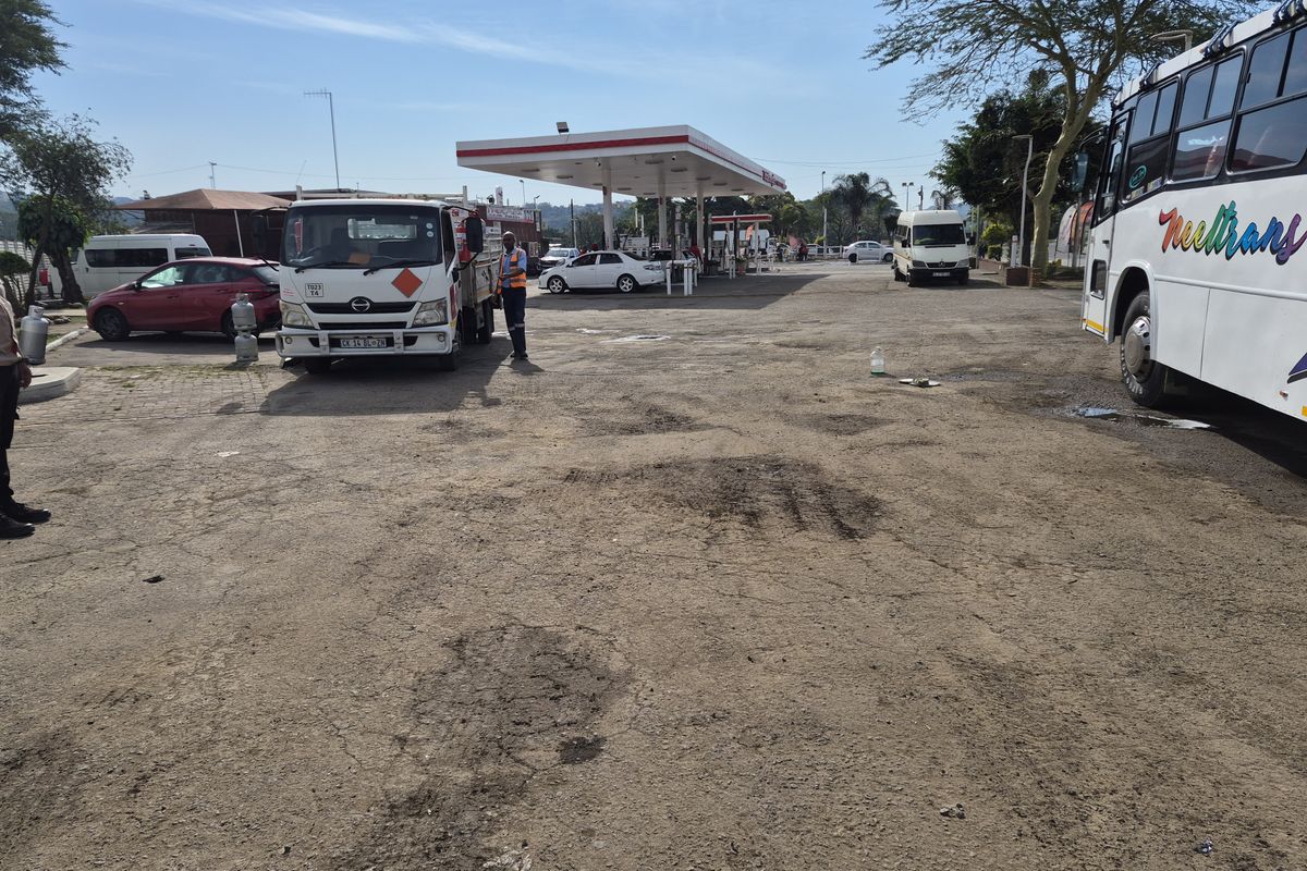 Commercial fuel station forecourt featuring a canopy, fuel pumps, and a paved surface area showing signs of wear.