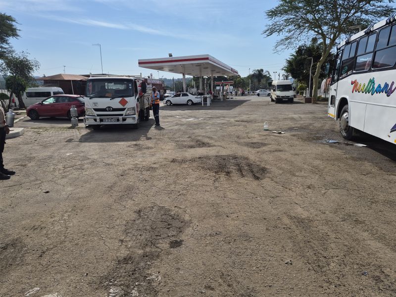 Commercial fuel station forecourt featuring a canopy, fuel pumps, and a paved surface area showing signs of wear.