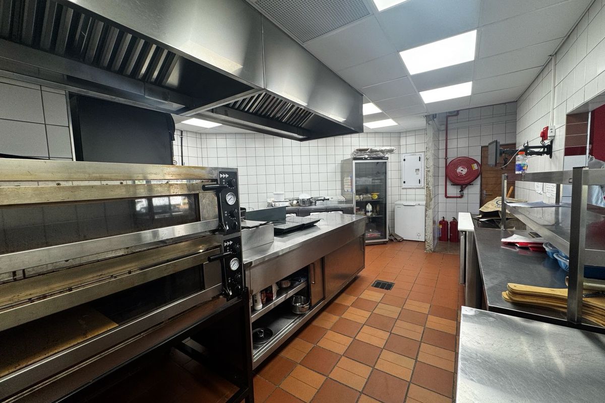 Commercial kitchen facility featuring stainless steel ovens, extractor hoods, prep counters, tiled surfaces, and integrated fire safety equipment.