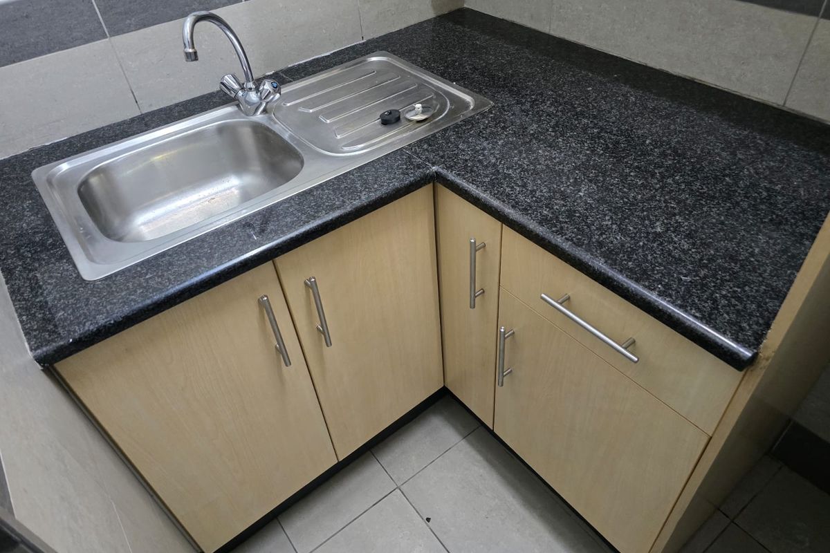 A compact kitchen kitchenette featuring light wood-finish cabinetry, a dark granite countertop, and a stainless steel sink with tiled backsplash.