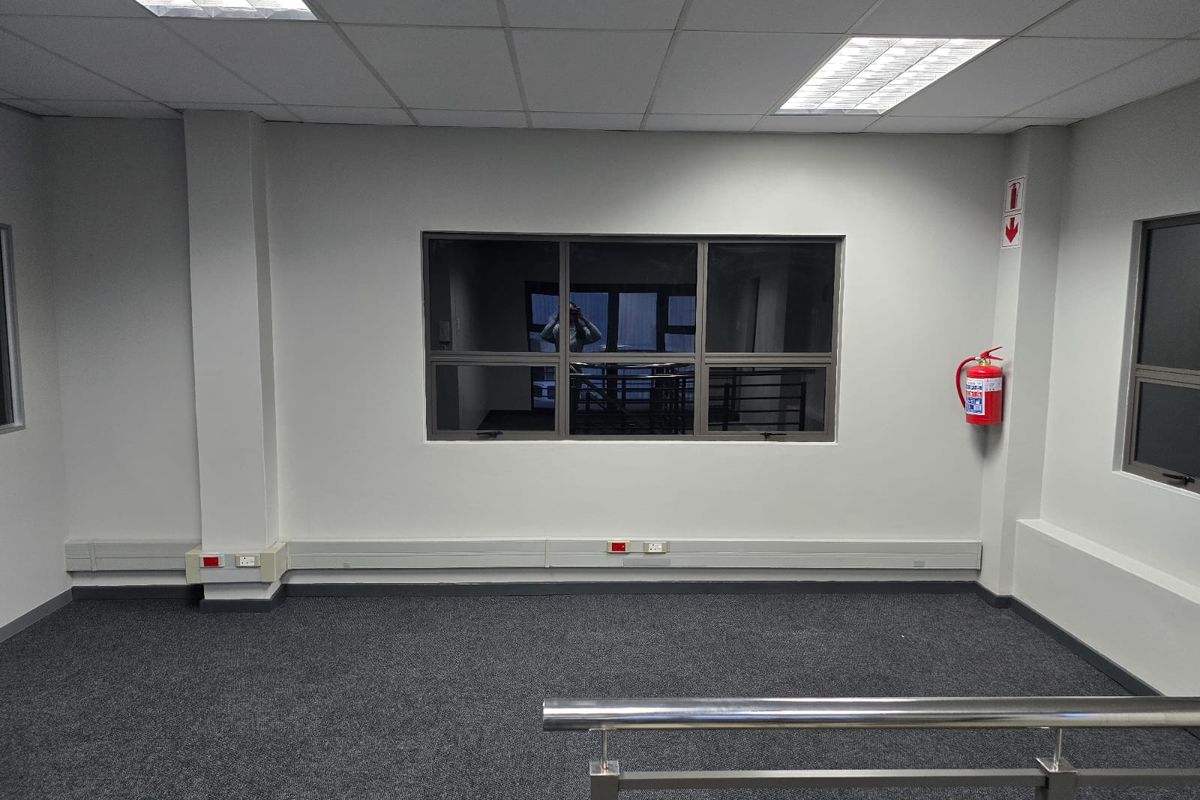 A clean, empty office space featuring carpeted flooring, suspended ceiling with recessed lighting, and integrated electrical trunking.