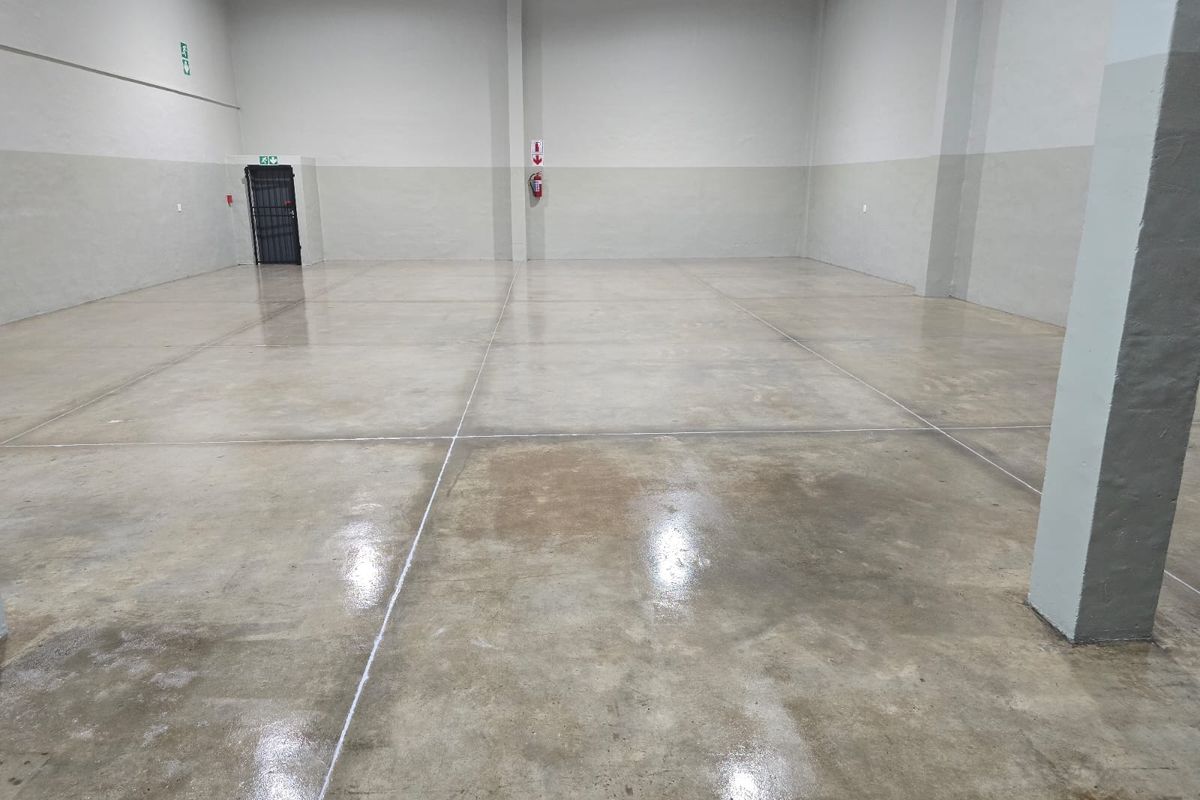 A spacious, clean industrial warehouse unit featuring polished concrete flooring, structural columns, and a secure access door.