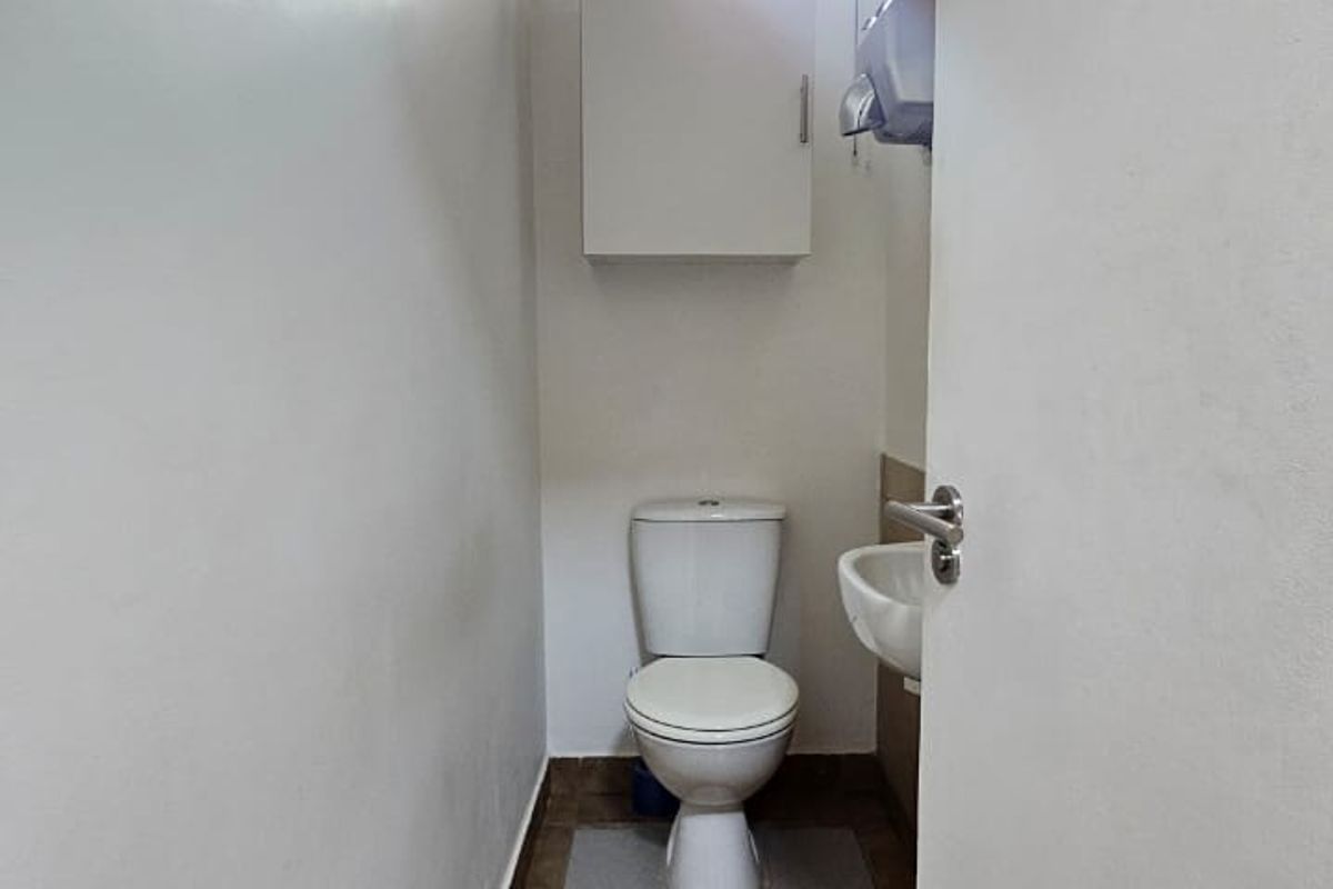 A compact office restroom featuring a standard toilet, wall-mounted basin, and storage cabinet with tiled flooring.