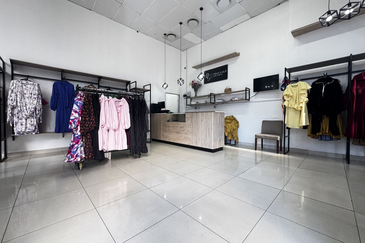 A bright retail boutique space featuring tiled flooring, a built-in service counter, wall-mounted shelving, and modern pendant lighting.