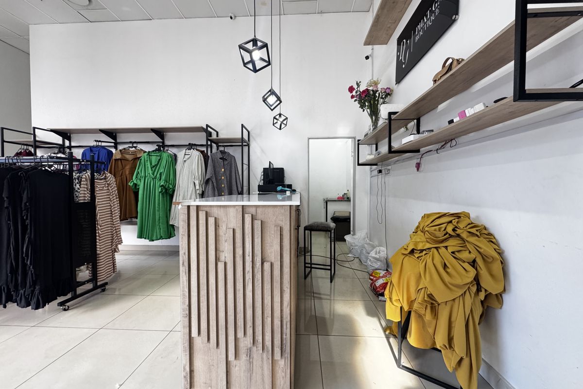 A retail boutique space featuring tiled flooring, modern pendant lighting, a service counter, and wall-mounted shelving units for product display.