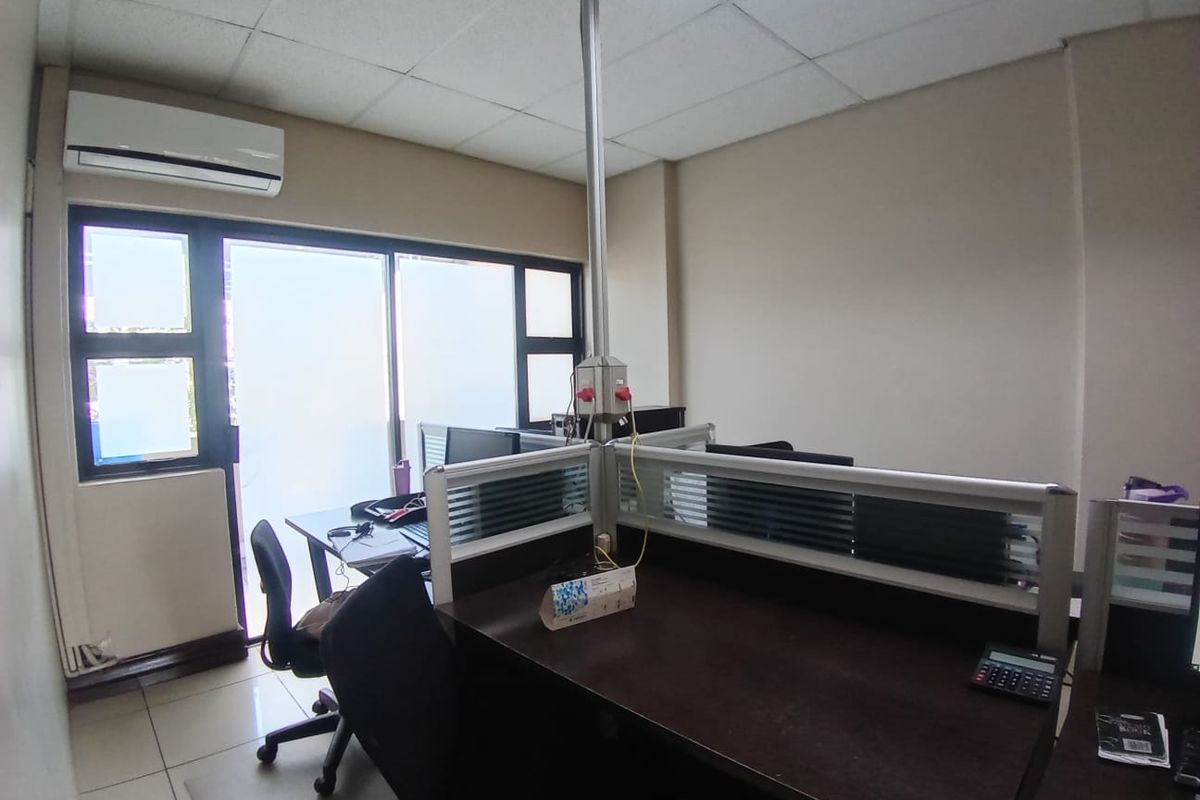 A functional office space featuring tiled flooring, a suspended ceiling, split-system air conditioning, and a sliding glass door providing natural light.