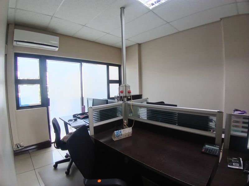 A functional office space featuring tiled flooring, a suspended ceiling, split-system air conditioning, and a sliding glass door providing natural light.