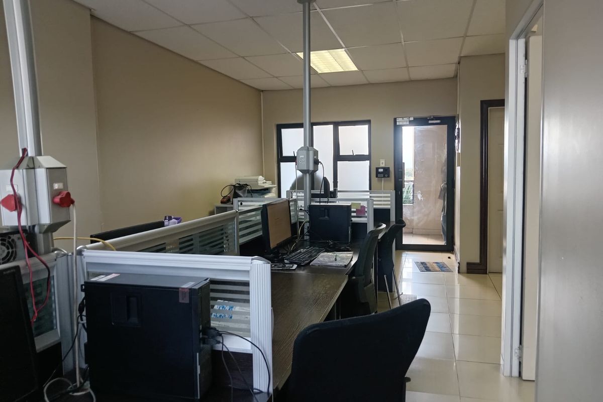 A functional office space featuring tiled flooring, suspended ceiling tiles, and direct access to an outdoor balcony area.