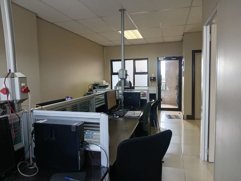 A functional office space featuring tiled flooring, suspended ceiling tiles, and direct access to an outdoor balcony area.