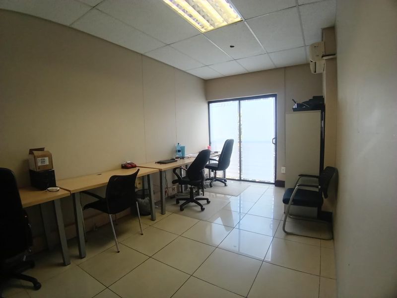 A functional office space featuring tiled flooring, a suspended ceiling with integrated lighting, and a sliding glass door providing natural light.
