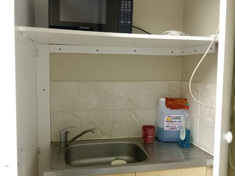 A compact scullery or utility area featuring a stainless steel sink, tiled splashback, and built-in cabinetry with dedicated microwave storage.